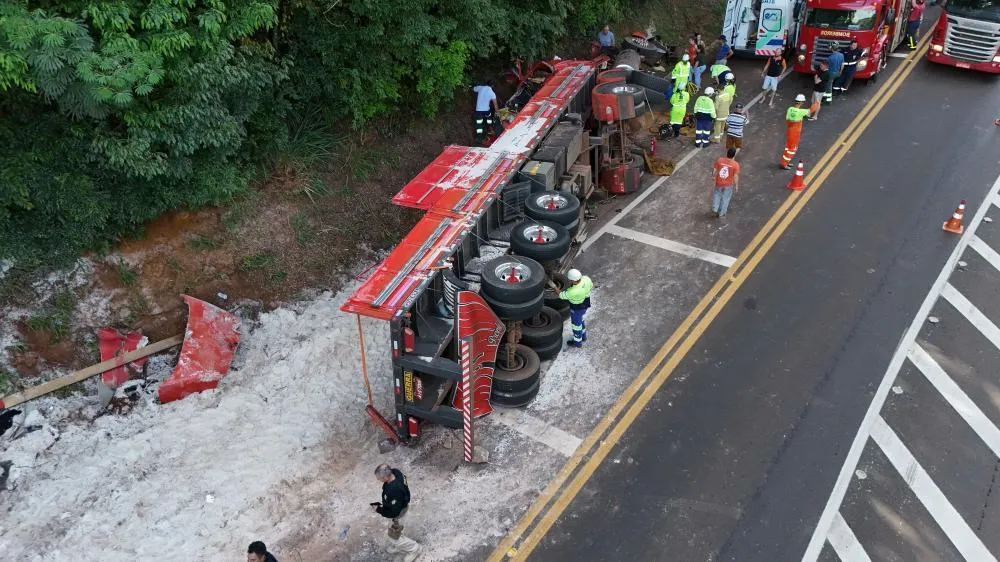 Imagem aérea mostra o caminhão tombado no km 418 da BR-277, com areia espalhada e equipes do Corpo de Bombeiros, PRF e EPR trabalhando no resgate do motorista preso às ferragens. Foto: Fabricio Eduardo - Portal do Paraná